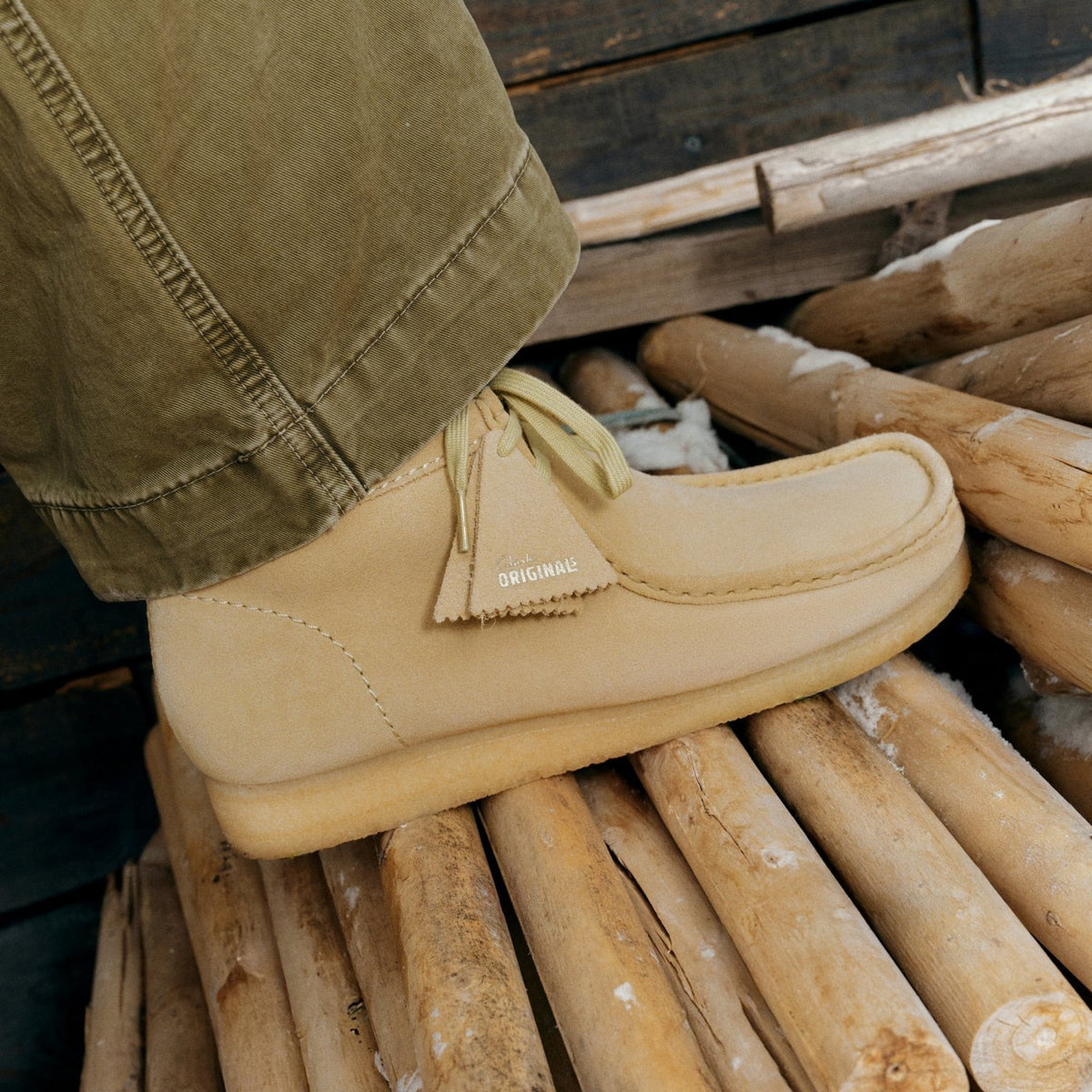 Clarks Wallabee on foot, Maple Suede upper with crepe sole and Originals tag, worn with olive pants on wooden logs