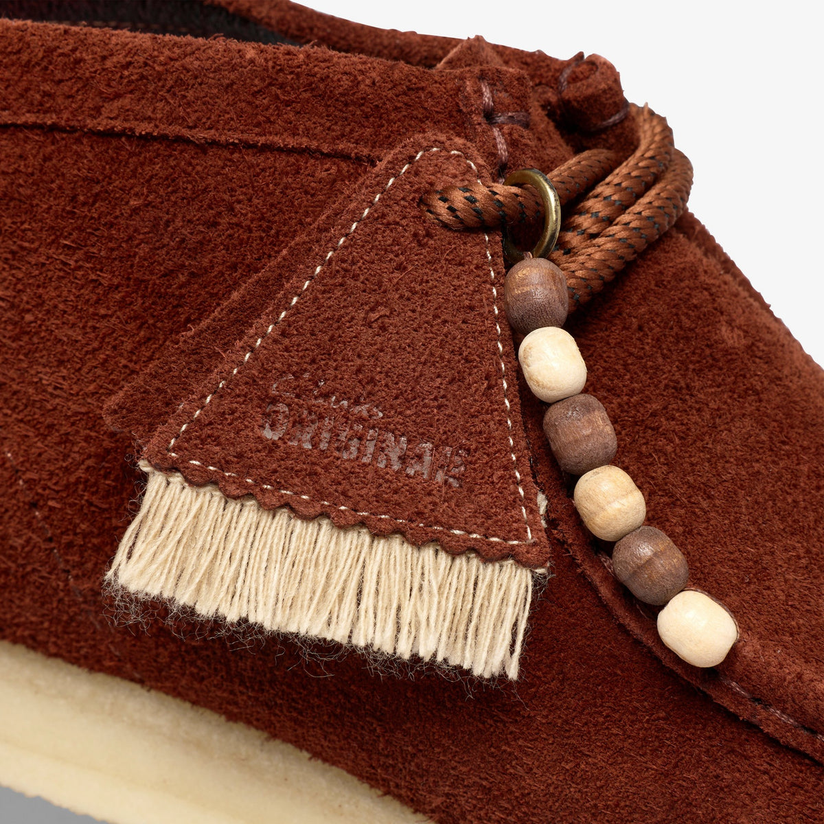 Clarks Wallabee close-up of Brown Combination Suede tag with Clarks Originals logo, cream fringe and wooden beads