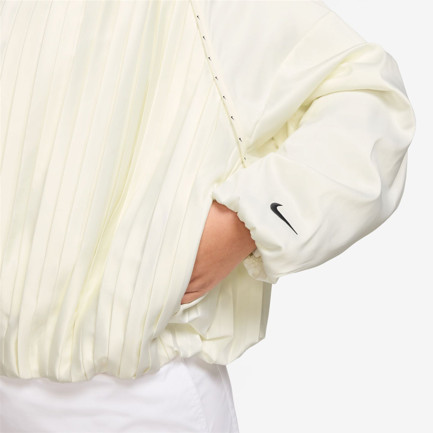 Close-up of a person wearing a cream-colored jacket with a Nike logo on the wrist on a white background