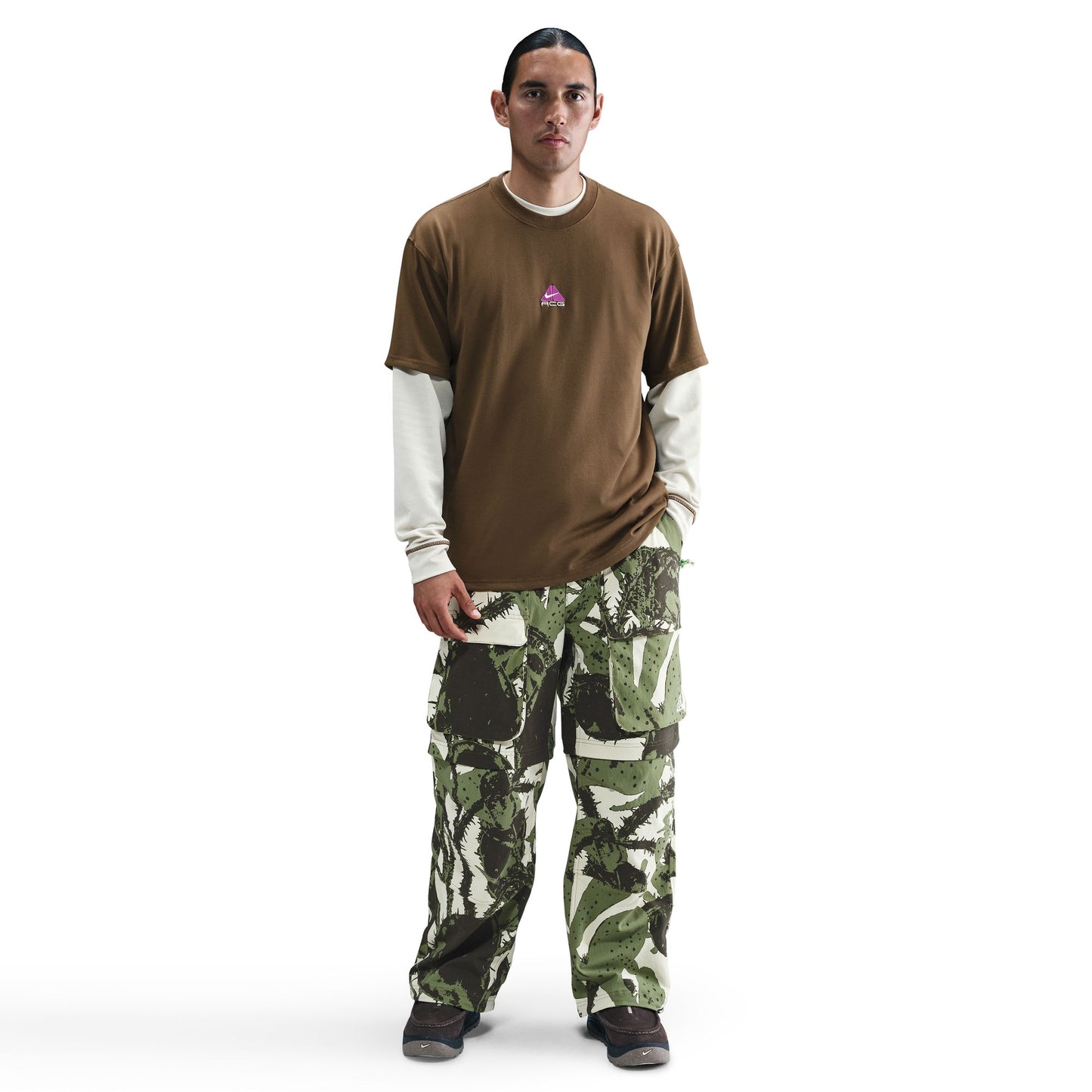 Man wearing a brown shirt and camouflage pants on a white background