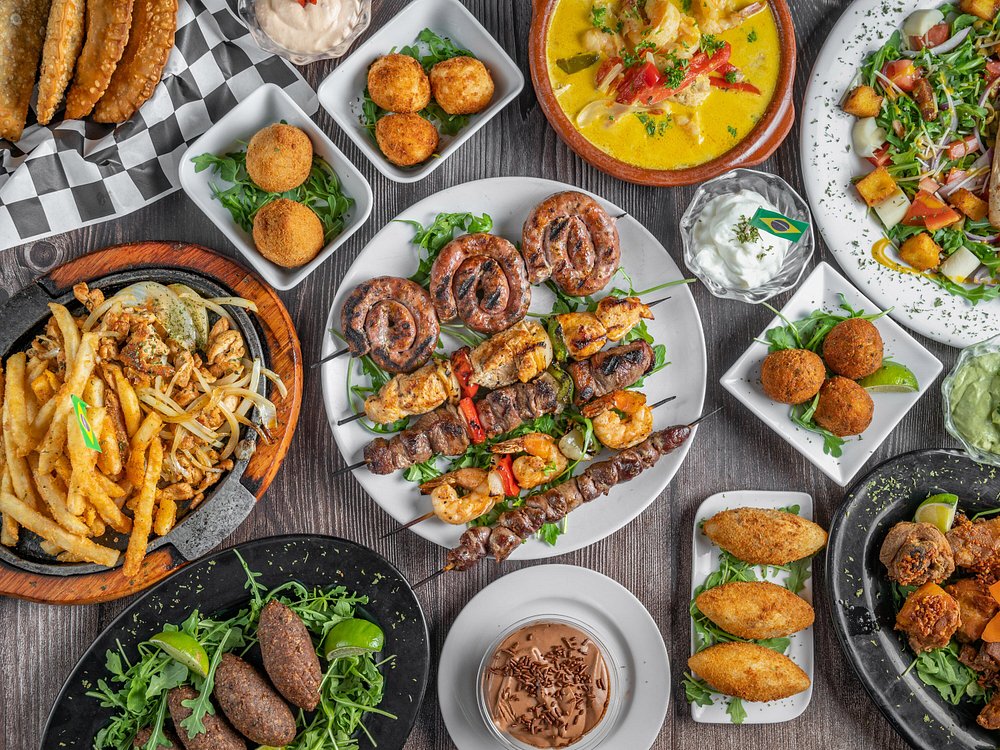 Spread of Boteco dishes: sausage, shrimp and meat skewers, croquettes, coxinhas, kibbeh, pastéis, loaded fries and moqueca