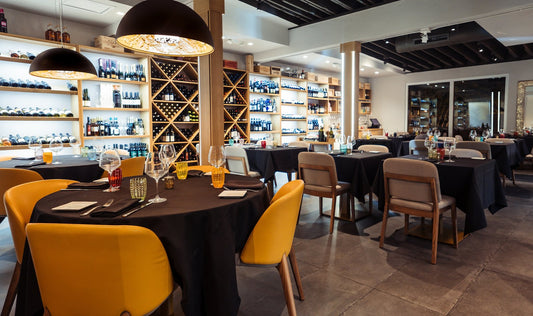Ferraro's Kitchen dining room with black-clothed tables, mustard leather chairs, dome pendant lamps and shelves of wine bottles