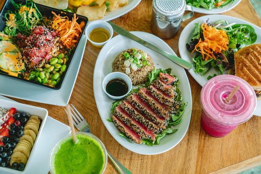 Overhead spread at Guarapo: sesame-crusted tuna on arugula with quinoa, a poke bowl, salad, a fruit bowl, green juice and a pink smoothie