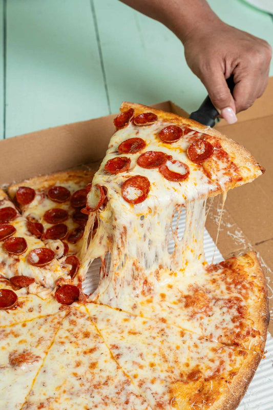 A hand lifts a pepperoni slice from a half pepperoni, half cheese pizza in its box, melted mozzarella stretching below