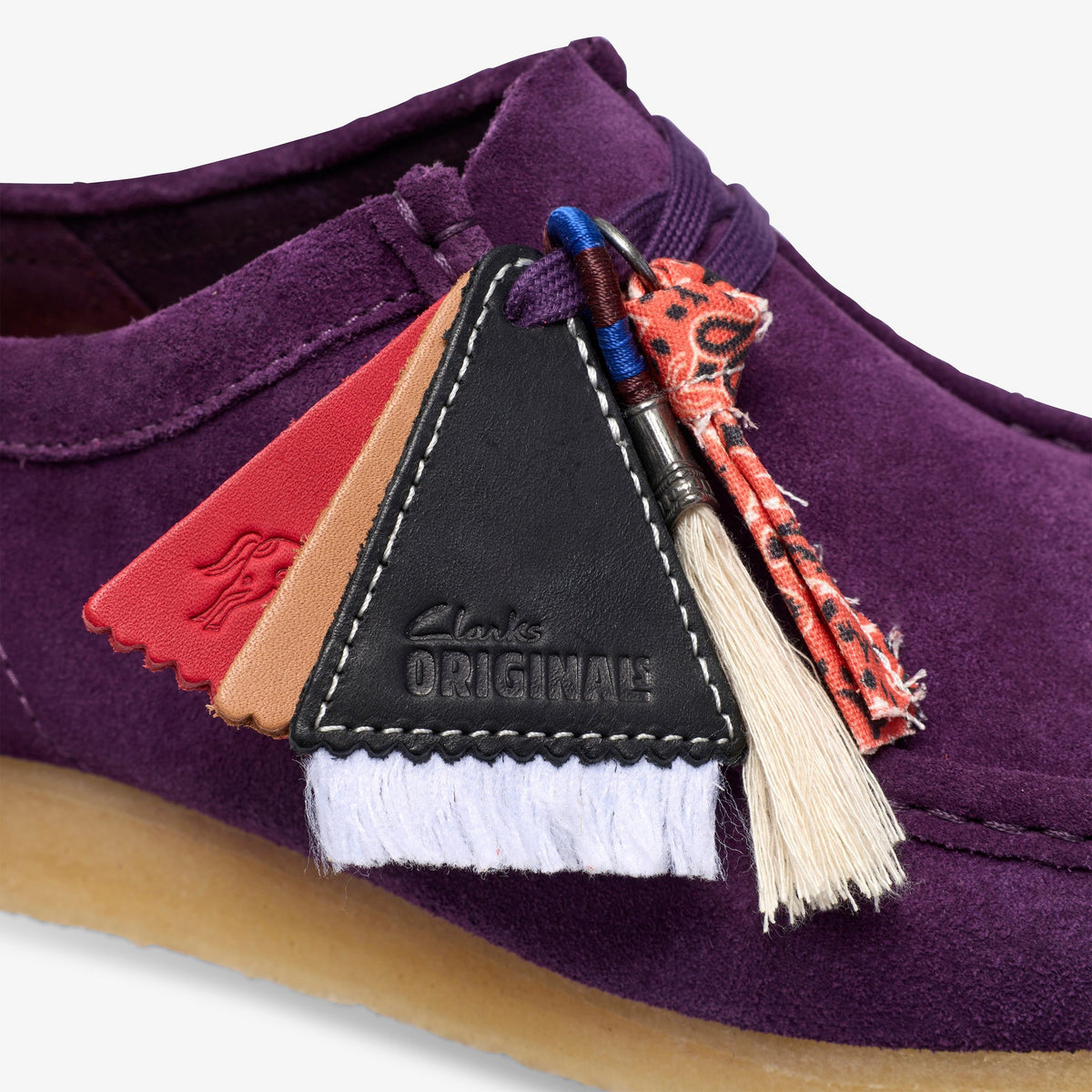 Clarks Wallabee close-up of black Clarks Originals leather tag, red and tan tags, tassels on Damson Suede