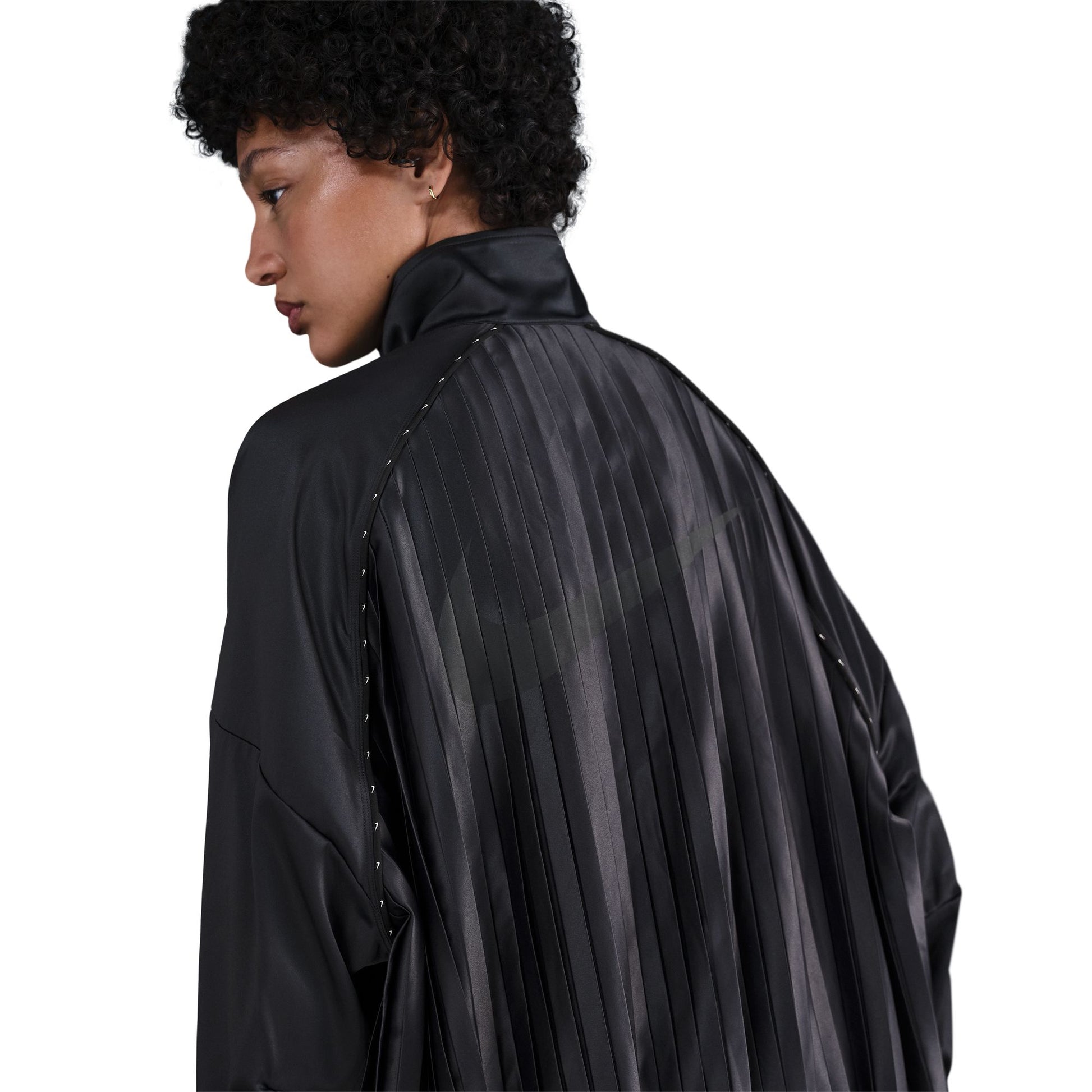 Person wearing a black satin pleated jacket with sheer panels on a white background