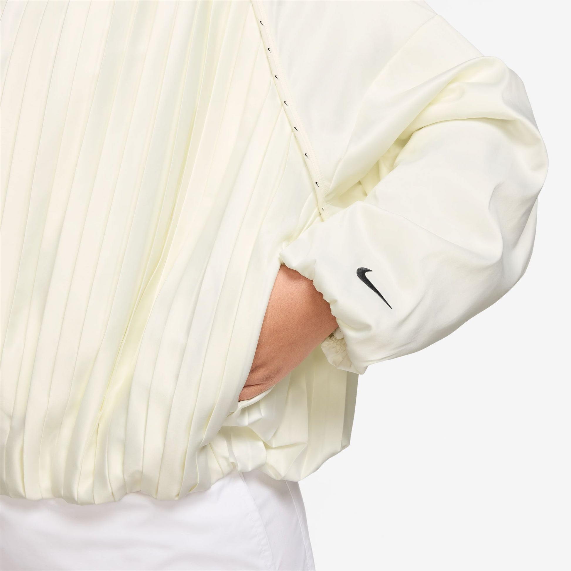 Close-up of a person wearing a cream-colored jacket with a Nike logo on the wrist on a white background