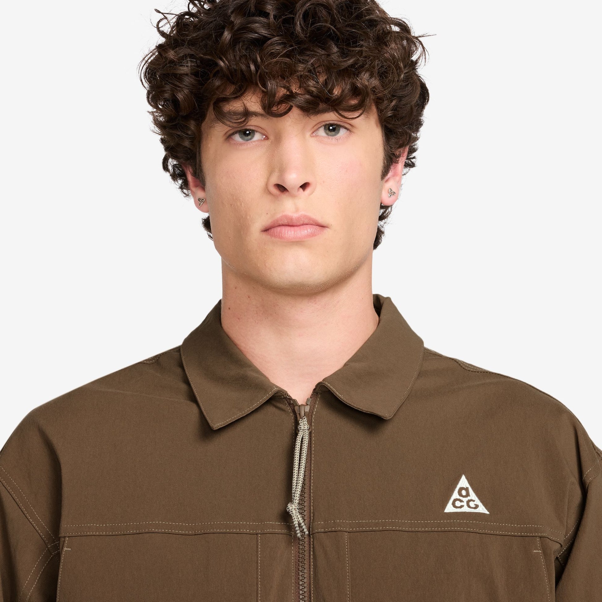 Person wearing a brown jacket with a Nike ACG logo on a white background