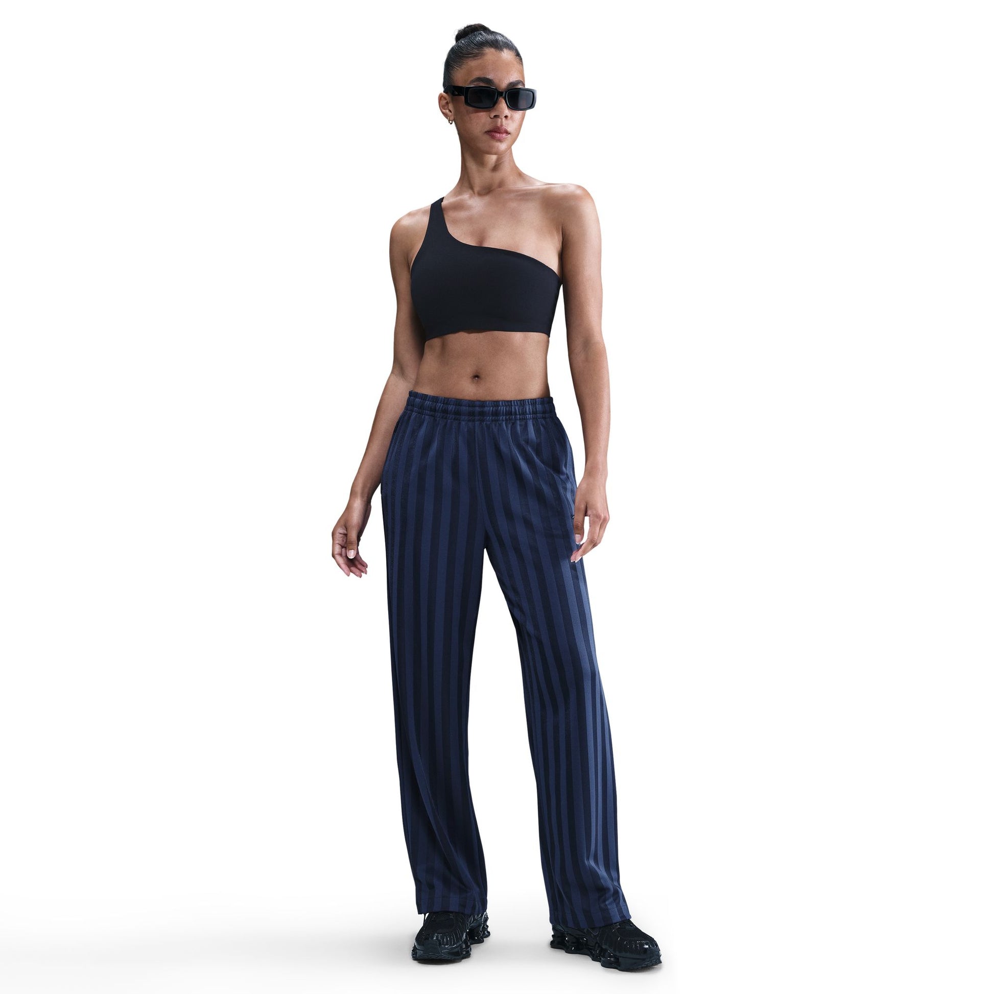Woman wearing a black one-shoulder top and blue striped pants on a white background