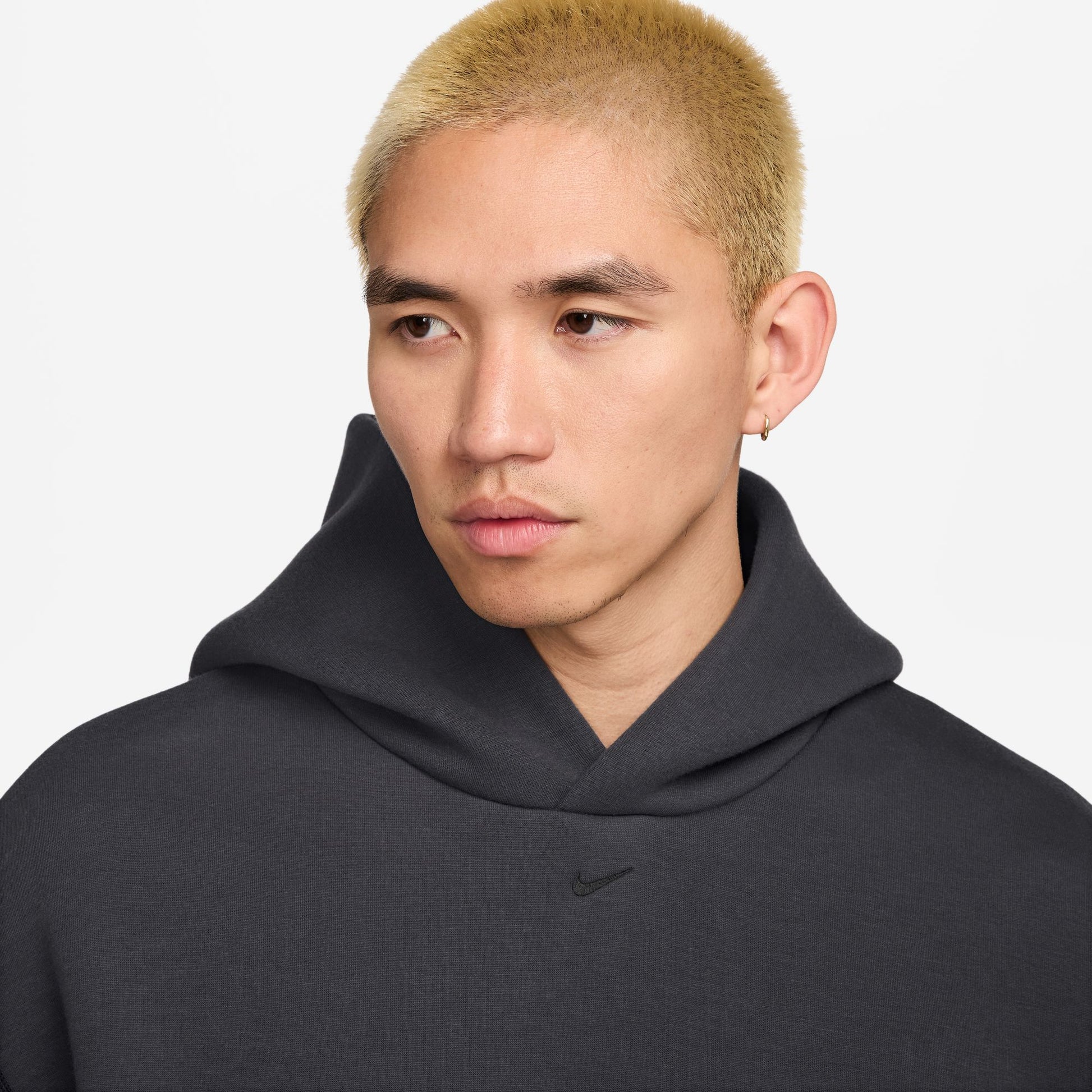 Person wearing a dark gray almost black hoodie with a Nike logo on a light gray background